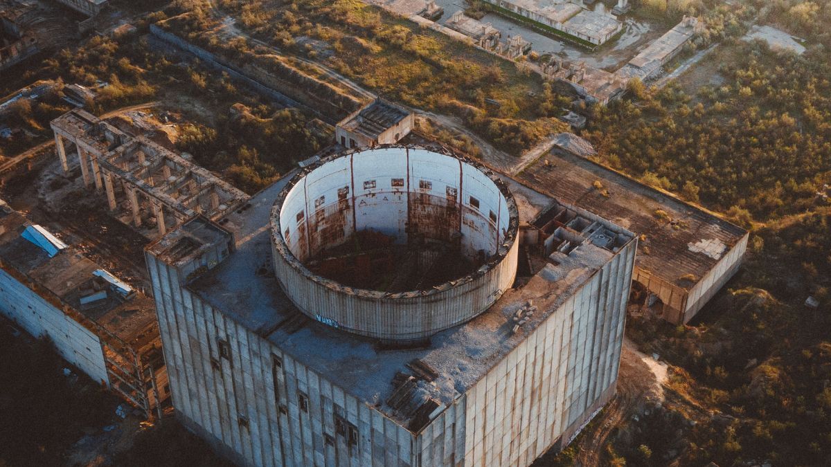 Agence internationale de l’énergie atomique : missions et importance Vue aérienne d'une centrale nucléaire abandonnée, avec des structures rouillées et des végétaux environnants.
