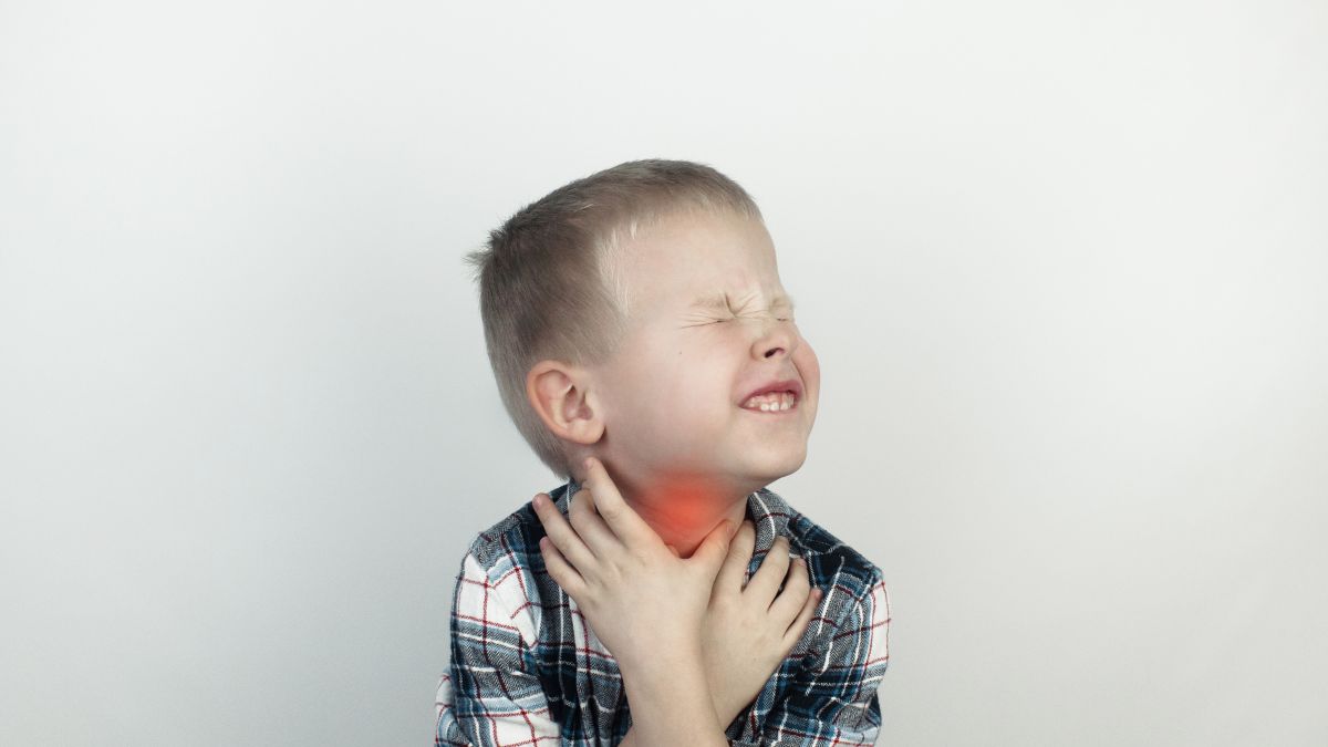 Un enfant grimace en se tenant la gorge, illustrant une douleur potentielle.