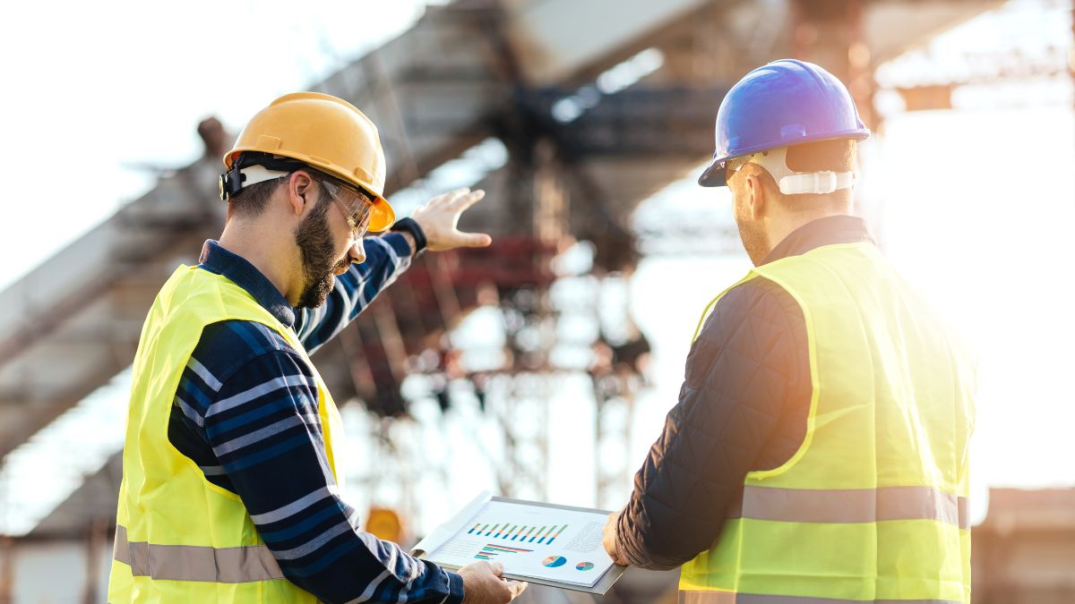 Deux travailleurs sur un chantier discutent des plans de construction avec des graphiques.