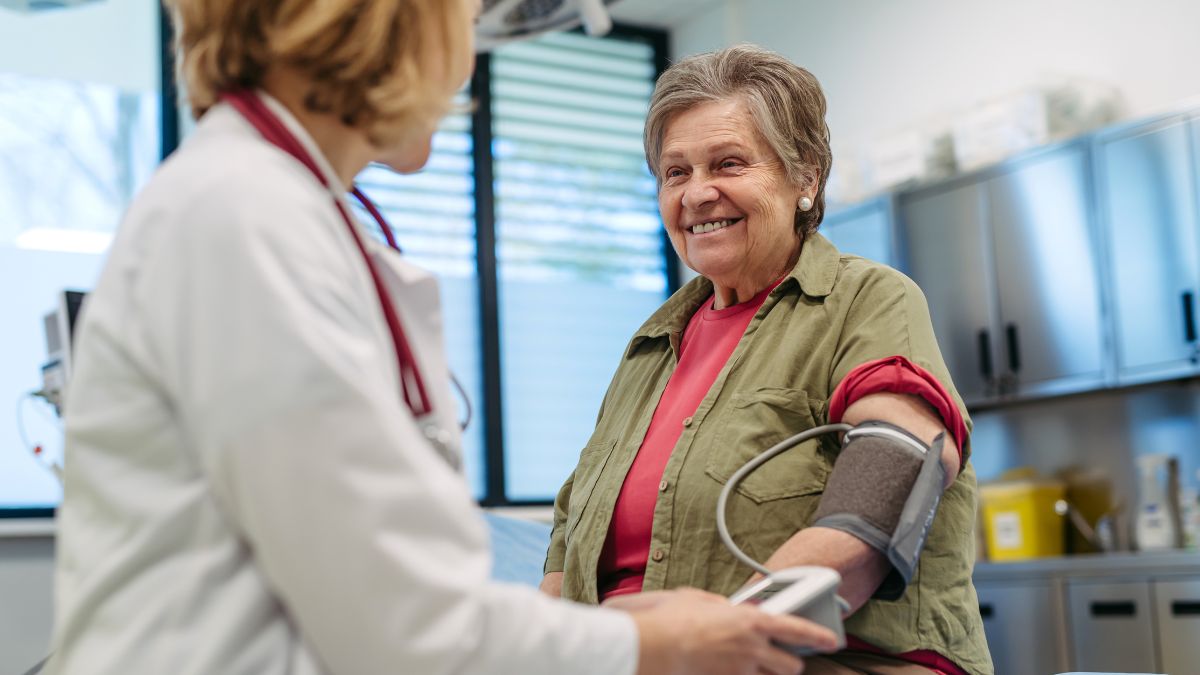 Chaleur et tension artérielle : ce que tu dois absolument savoir Une femme âgée souriante se fait mesurer la tension artérielle par un médecin.