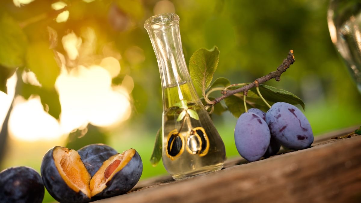 Une bouteille d'eau-de-vie à côté de prunes fraîches sur une table en bois.
