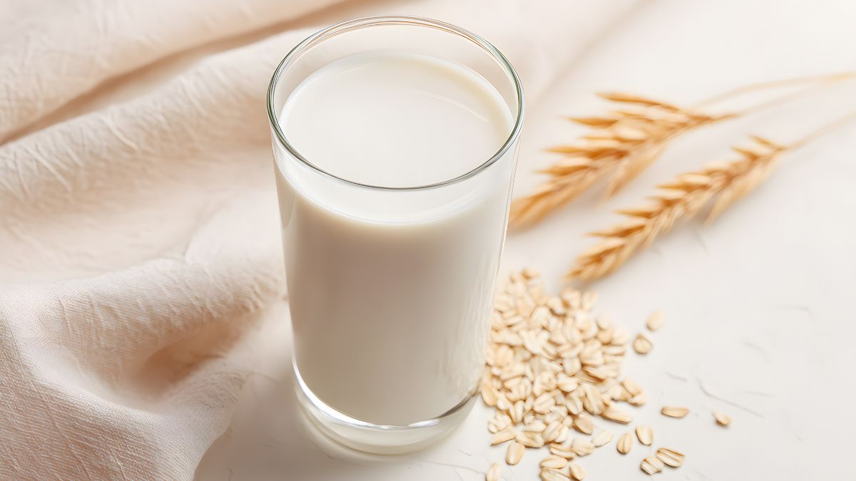 Un verre de lait d'avoine sur une nappe claire, avec des flocons d'avoine à côté.