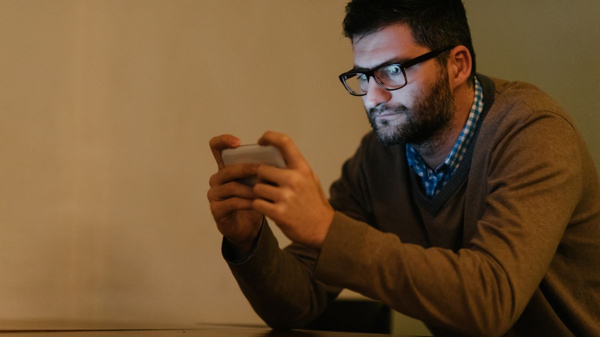 Un homme regardant son téléphone dans une pièce sombre, absorbé par l'écran.