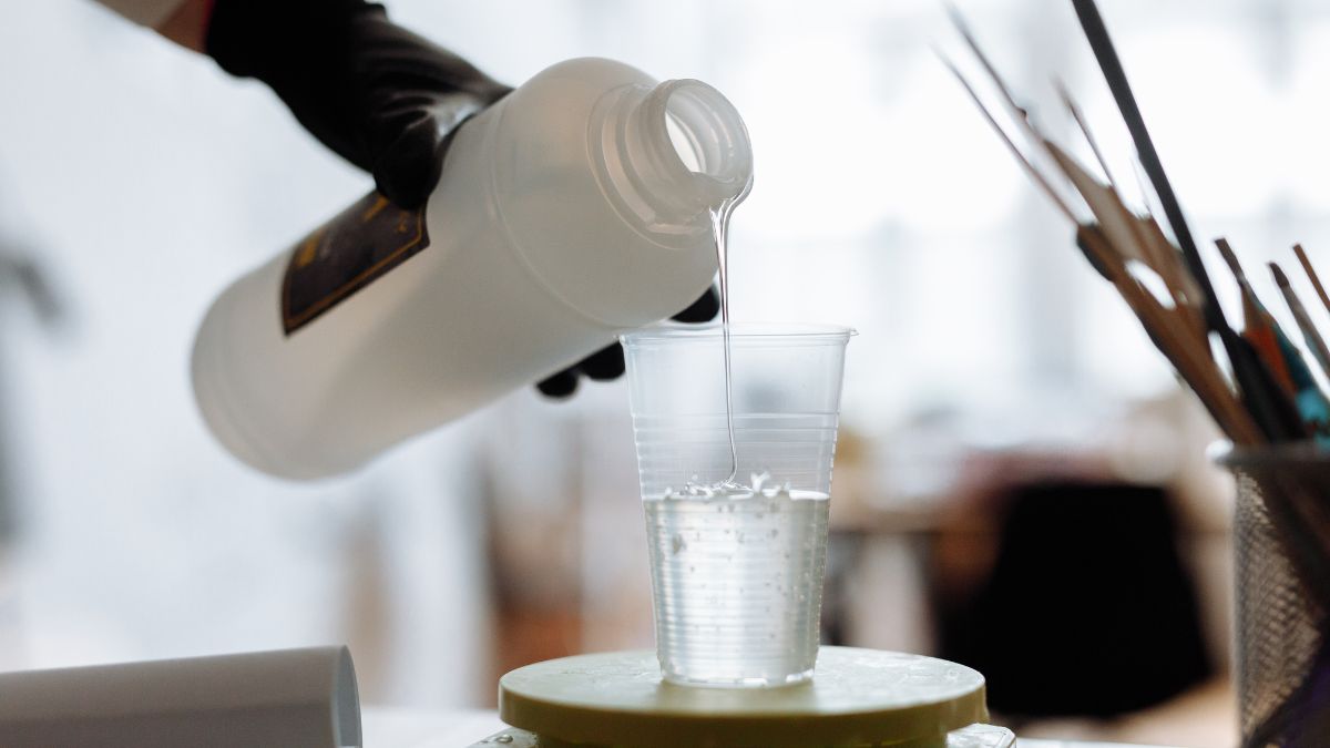 Un flacon verse un liquide clair dans un gobelet en plastique, illustrant une préparation.