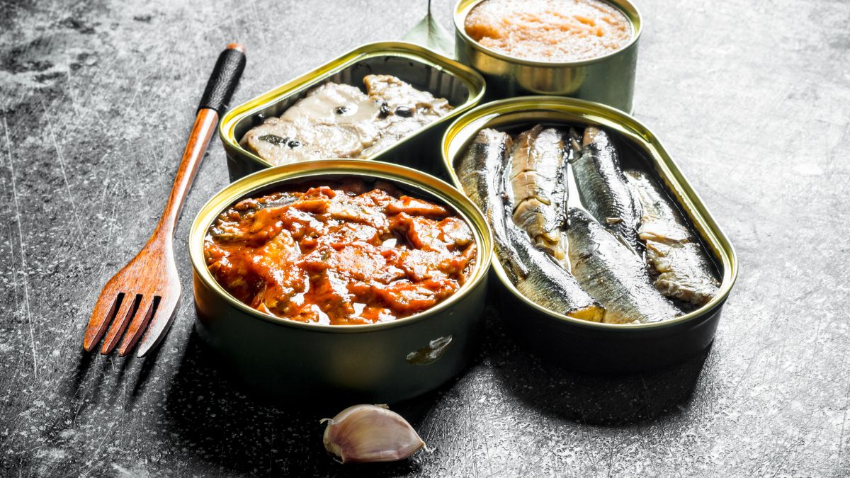 Des boîtes de conserve contenant divers poissons et fruits de mer, avec une fourchette en bois à côté.