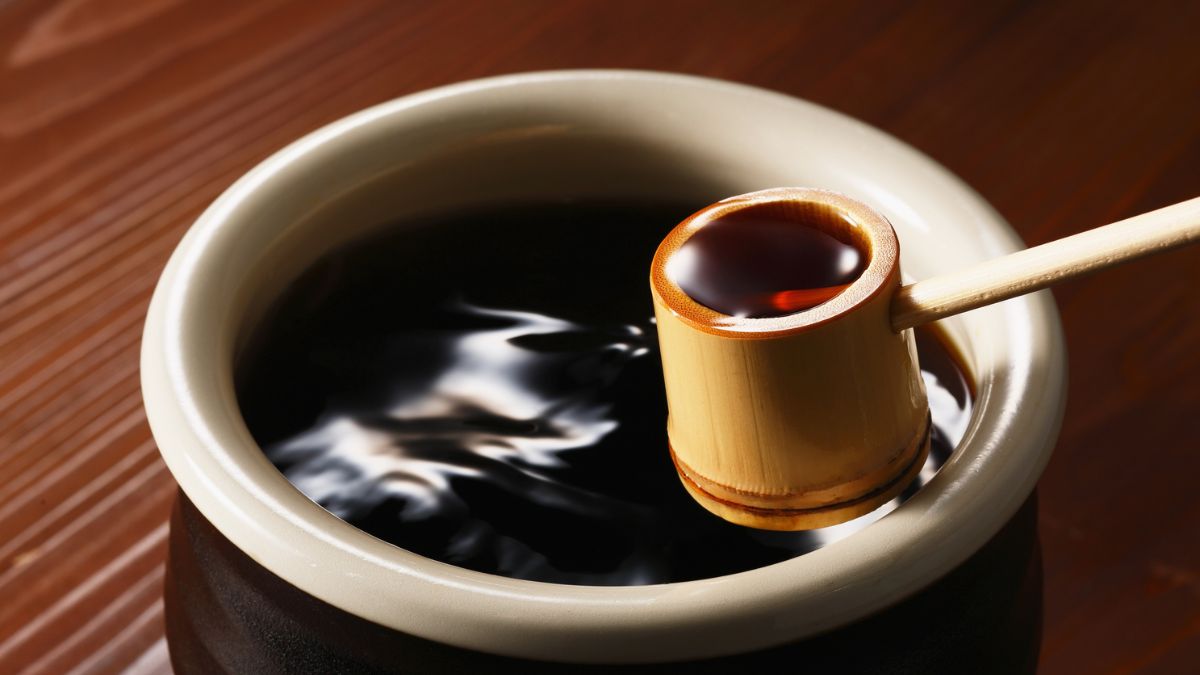 Un bol en céramique contenant une sauce sombre, avec une cuillère en bambou.