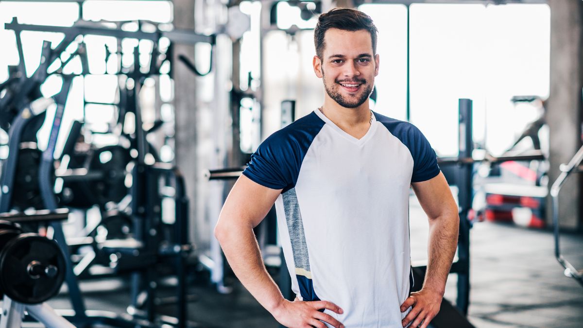 Un homme souriant en tenue de sport dans une salle de gym moderne.