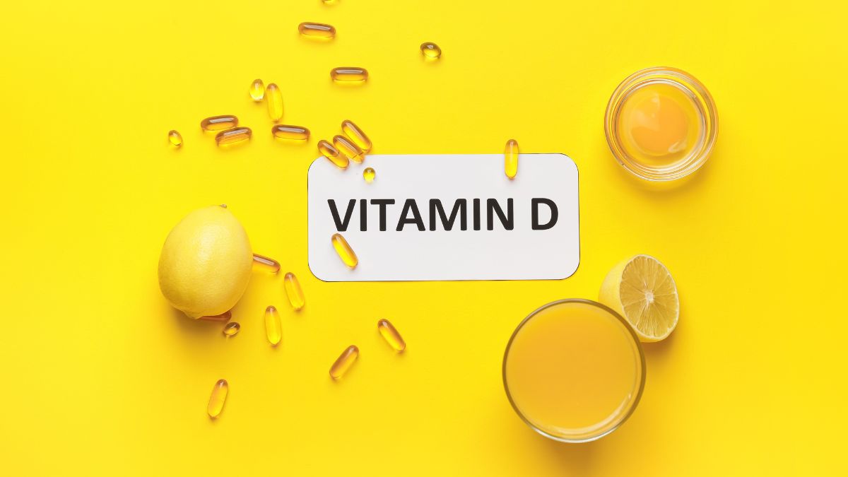 Des gélules de vitamine D, un citron et un verre de jus sur fond jaune.