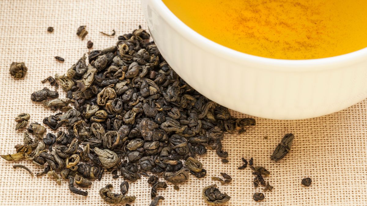 Des perles de thé Gunpowder et une tasse de thé infusé sur une nappe beige.